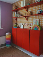 Ockergelbe Gingham-Tapete von Atelier Chien hinter einem roten Schrank und Wandregalen.