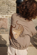 Thermo jacket Juno Bomber – Walnut – Konges Sløjd: detail of the leopard artwork on the back of the bomber jacket being worn.